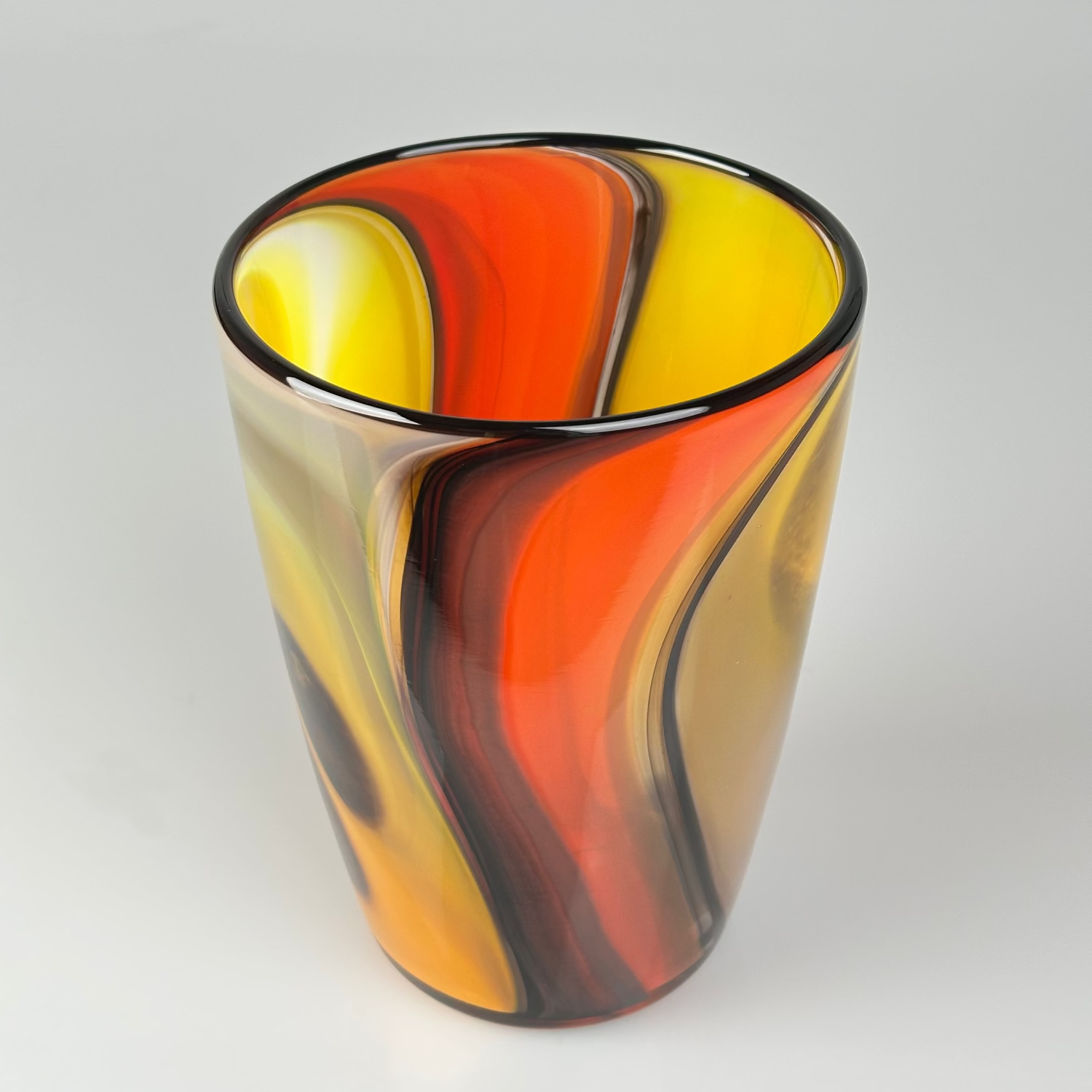 A hand-blown glass vase with a marbled swirl pattern of orange, yellow, brown, and black on a light gray background.